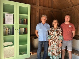 Bücherschrank Wollomoos 3 Personen im Marktplatz, vor einem Bücherregal.