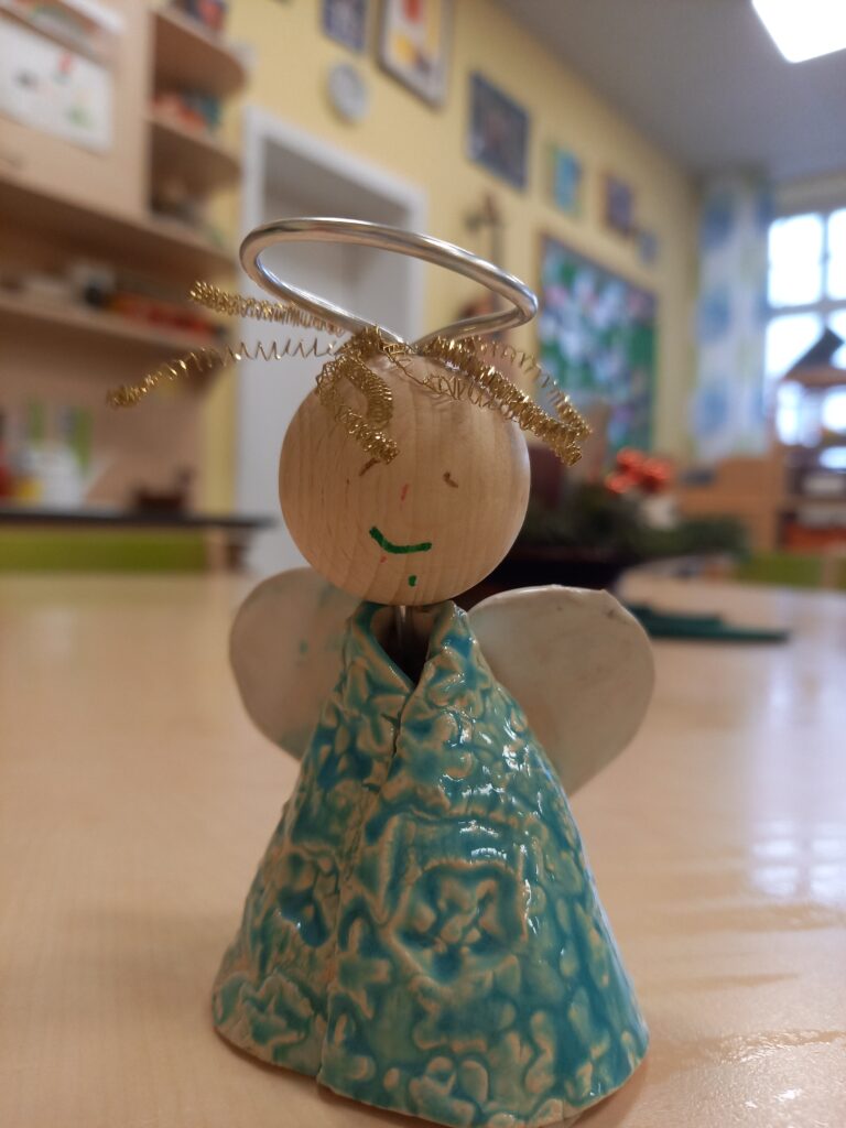 engel Holzangelt mit glasigem Körper und goldener Schleife auf der Stirn.