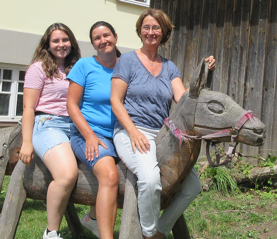 Mutter und zwei Kinder auf einem Holz-Pferd im Garten.